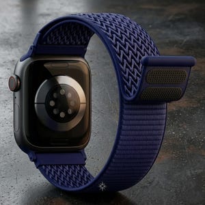 Puede incluir: Un reloj inteligente gris oscuro con una correa de nailon tejido azul marino. La esfera del reloj es negra con un acento rojo en el lateral. La correa presenta un patrón texturizado y un cierre seguro. El reloj está diseñado para el fitness y el uso diario.