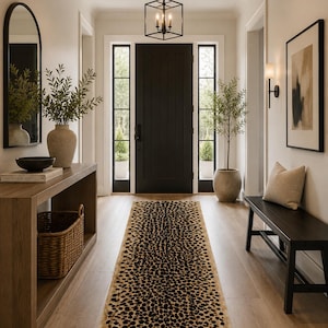 May include: A rectangular runner rug featuring a tan background with a repeating black leopard print pattern. The rug is positioned on a light wood floor in a hallway leading toward a black front door with glass side panels and a metal light fixture.