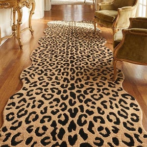 May include: A long, runner-style rug featuring a repeating black leopard print pattern on a tan background. The rug has an irregular, organic shape with curved edges that follow the contours of the animal-inspired spot design.