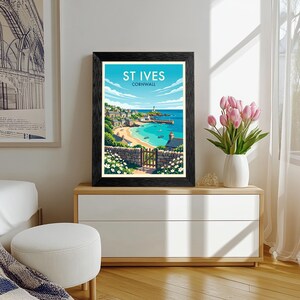 May include: A framed art print featuring a coastal landscape of St Ives, Cornwall, with a sandy beach, turquoise water, a lighthouse, and stone walls. The text 'ST IVES CORNWALL' is printed in white at the top of the illustration.