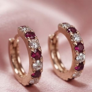 Könnte beinhalten: Ein Paar Creolen aus Roségold mit einem abwechselnden Muster aus rund geschliffenen, tiefroten Rubinen und klaren weißen Diamanten, die entlang der Vorderkante jedes kreisförmigen Rings gefasst sind und ein symmetrisches Schmuckdesign bilden.