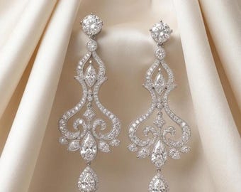 May include: A pair of silver-toned chandelier earrings featuring a round stud top, a marquise-cut stone in the center, and a dangling pear-shaped drop at the bottom. The entire structure is encrusted with numerous small, clear, sparkling stones.