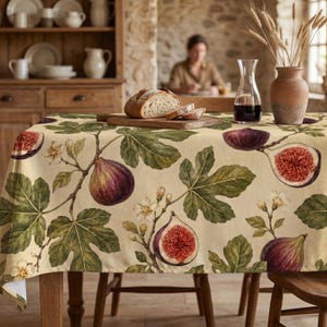 May include: A rectangular tablecloth featuring a botanical print of dark purple figs, green fig leaves, and small white flowers on a cream-colored background. The fabric covers a wooden table, displaying a repeating pattern of whole and sliced figs.