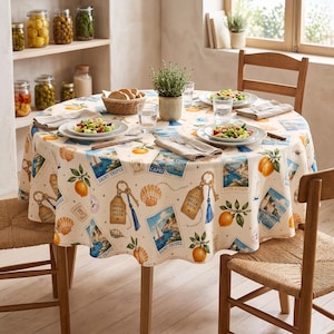 May include: A round tablecloth featuring a cream background with a repeating pattern of lemons, seashells, blue tassels, and vintage-style postcards depicting Saint-Tropez, Capri, and Cote d'Azur, along with luggage tags labeled Hotel Bella Vista.