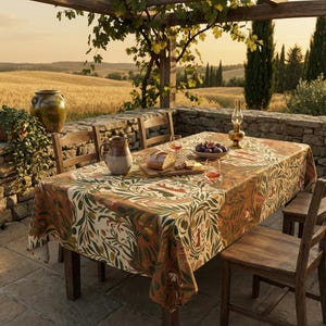 May include: A rectangular tablecloth with a botanical design in shades of orange, green, and cream covers a wooden table set for dining. The table is set outdoors with food and drinks, and wooden chairs.