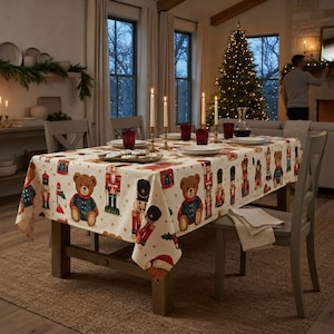 May include: A rectangular tablecloth featuring a repeating pattern of brown teddy bears wearing blue sweaters and red nutcracker figures on a cream background. The fabric is draped over a wooden dining table set with plates and candles.