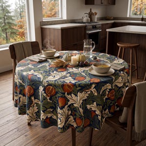 May include: A round tablecloth featuring a dark blue background with a repeating pattern of orange pomegranates, green leaves, and small birds. The table is set with two bowls of soup, a glass pitcher of water, a white candle, and two small pumpkins.