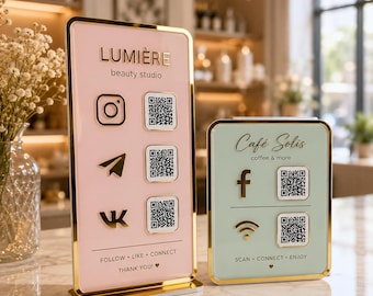 Op de afbeelding: Twee rechthoekige acrylborden met gouden randen. Het hogere roze bord toont LUMIÈRE beauty studio met sociale media iconen en QR-codes. Het kortere mintgroene bord toont Café Solis coffee & more met sociale media iconen en QR-codes.