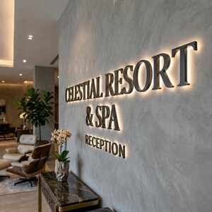Op de afbeelding: Een wandbord met verlichte zwarte letters met de tekst CELESTIAL RESORT & SPA RECEPTION, gemonteerd op een grijs gestructureerd oppervlak. Het bord heeft een gloeiend halo-effect achter elke letter voor een hoog contrast.