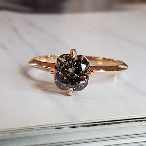 Peut inclure: Une bague en or rose ornée d'un diamant brun foncé taille coussin monté sur quatre griffes. L'anneau présente une finition polie et un design effilé qui mène à la pierre centrale, créant une apparence élégante et raffinée pour ce bijou.