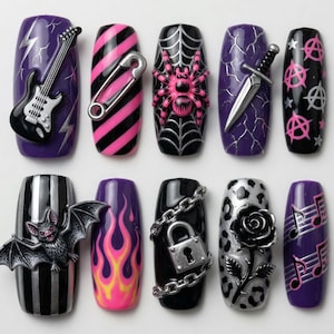 May include: A collection of ten artificial nails with various designs. The designs include a black guitar, a safety pin, a pink spider on a web, a dagger, anarchy symbols, a bat, flames, a padlock, a rose, and musical notes.