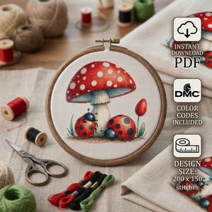 Puede incluir: Un patrón de punto de cruz con una seta roja grande de puntos blancos y dos mariquitas sobre tela blanca, en un bastidor de madera circular. El diseño incluye texto que indica descarga instantánea en PDF, códigos de color DMC y un tamaño de diseño de 200 x 150 puntos.