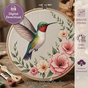 Puede incluir: Un patrón de punto de cruz en un bastidor de madera con un colibrí de plumaje verde, blanco y rojo, rodeado de flores rosas y melocotón y hojas verdes. El diseño incluye texto que indica 200x200 puntadas y una descarga digital.