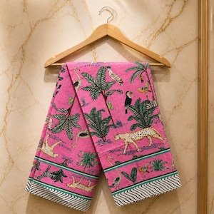 May include: A pink fabric with a jungle-themed print featuring leopards, birds, and palm trees. The fabric is hanging on a wooden hanger. The design includes a border with black and white stripes and green accents.