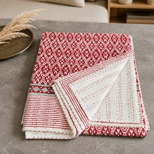 May include: A folded cotton quilt featuring a red and white diamond pattern on one side and a white surface with red stitched lines on the reverse. The textile displays intricate kantha-style running stitch details throughout the fabric.