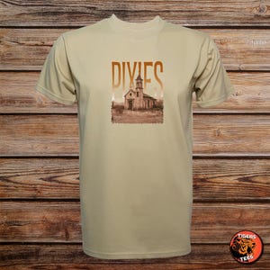 May include: A beige t-shirt with a sepia-toned image of a church and the word "DIXIES" in a copper colour. The shirt is made of a soft material and has short sleeves.