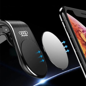 May include: A black and silver car phone mount with the Audi logo. The mount has a magnetic base and a separate metal plate. Blue arrows indicate the magnetic connection. A smartphone is visible in the background.