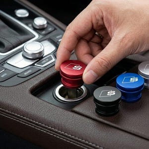 May include: A hand placing a red car accessory into a car's cigarette lighter port. The accessory has a silver "S" logo. Other accessories in black, blue, and silver are nearby.