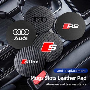 Może przedstawiać: Zestaw pięciu czarnych podkładek do samochodu z różnymi logo i emblematami Audi, w tym pierścieniami Audi, RS, S i S line. Podkładki mają fakturę włókna węglowego i są przeznaczone do uchwytów na kubki w samochodzie. Widoczny jest również tekst "Mugs Slots Leather Pad".