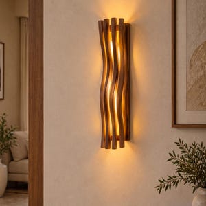 May include: A vertical wall sconce featuring a series of parallel, wavy wooden slats in a medium brown finish. The light fixture emits a warm, glowing light from behind the slats, casting soft shadows against the wall surface.