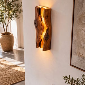 May include: A vertical wall-mounted light fixture crafted from a single piece of natural wood with a prominent central fissure. The wood features visible knots and a warm, golden-toned grain. An internal light source illuminates the gap.