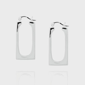 May include: A pair of shiny silver rectangular hoop earrings. The earrings have a polished finish and a simple, modern design. The hoops are approximately 1.5 inches long and 0.75 inches wide.