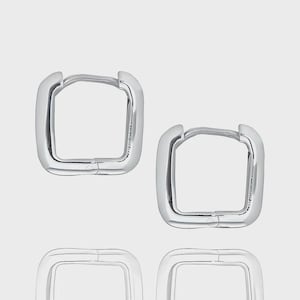 May include: A set of four silver-colored square hoop earrings. The earrings have a rounded, polished finish and a hinged closure. The design is minimalist and modern, suitable for everyday wear.