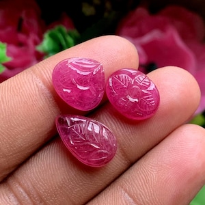 May include: Three small, vibrant pink gemstones with intricate carved leaf and floral patterns. Each stone features a polished, translucent surface with detailed engravings that highlight the natural depth and color of the pink material.