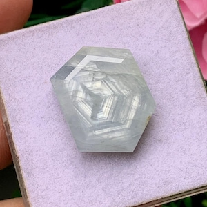 Peut inclure: Une pierre précieuse hexagonale bleu pâle translucide avec une surface plate et polie. La pierre présente des bandes géométriques internes distinctes et un motif à facettes net et clair qui crée un aspect cristallin superposé.