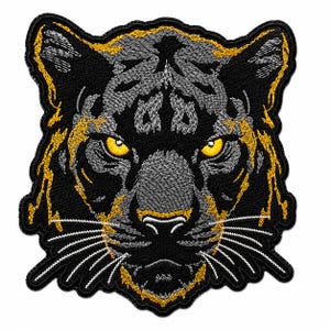 Könnte beinhalten: Ein gestickter Aufnäher mit einem Tigerkopf aus schwarzem, grauem und gelbem Garn. Das Design zeigt ein detailliertes Katzengesicht mit stechend gelben Augen, markanten weißen Schnurrhaaren und einem schwarzen Rand um die Form.