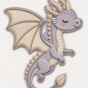 Könnte beinhalten: Ein gestickter Aufbügler in Form eines helllavendelfarbenen Drachen mit cremefarbenen Flügeln, Hörnern und Schwanzspitze. Der Drache hat geschlossene Augen, ein kleines Lächeln und rosa Wangen, mit detaillierten Stickereien im gesamten Design.