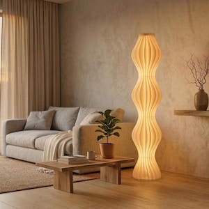 Peut inclure: Un lampadaire crème avec un design ondulé unique. La lampe est allumée, diffusant une lueur chaleureuse dans un salon. La hauteur de la lampe est d'environ 183 cm.