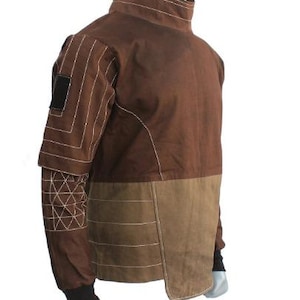 May include: Brown jacket with a high collar and contrasting tan panels. The jacket features white stitching details on the sleeves and body, with a black patch on the upper arm. The cuffs are black.