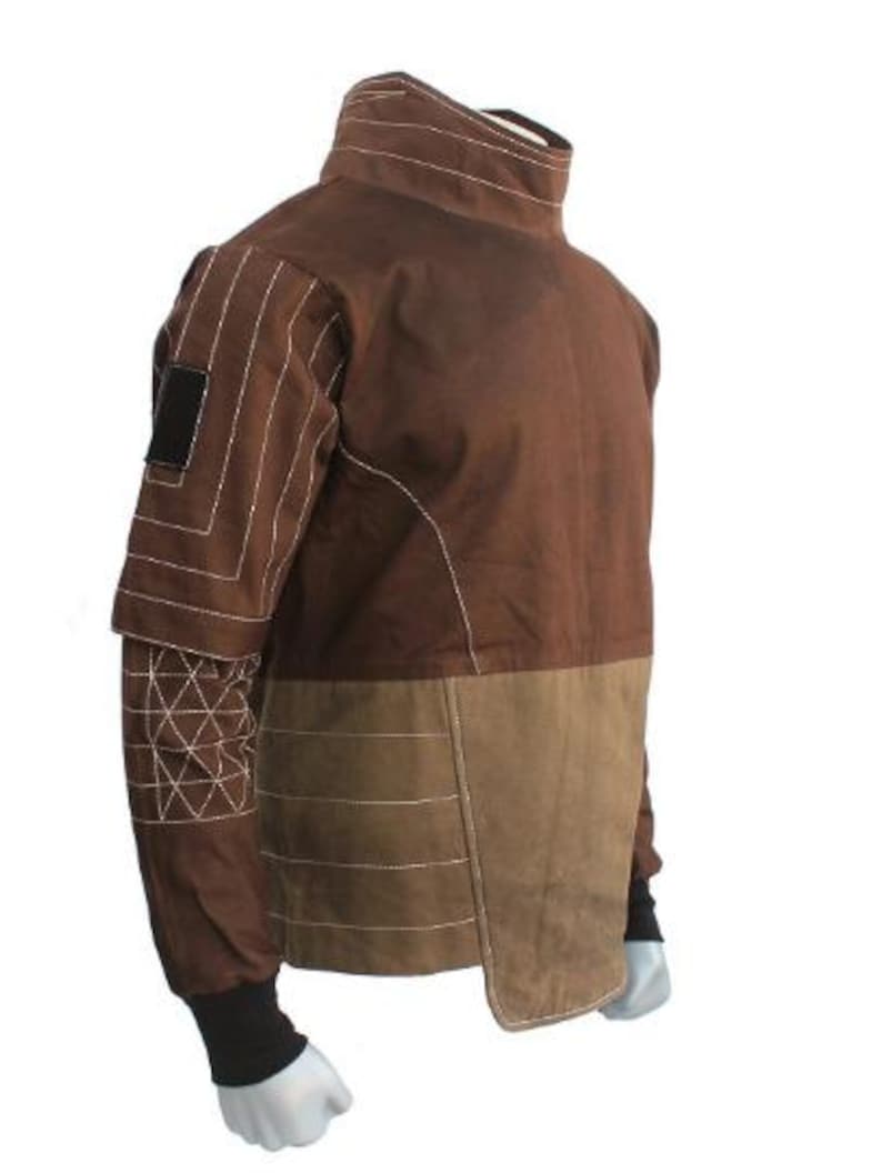 May include: Brown jacket with a high collar and contrasting tan panels. The jacket features white stitching details on the sleeves and body, with a black patch on the upper arm. The cuffs are black.