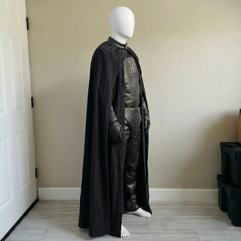 May include: A black costume displayed on a mannequin. The costume includes a long cape, a leather-like chest piece, pants, gloves, and a belt. The mannequin is wearing white shoes. The costume is designed for cosplay or costume parties.