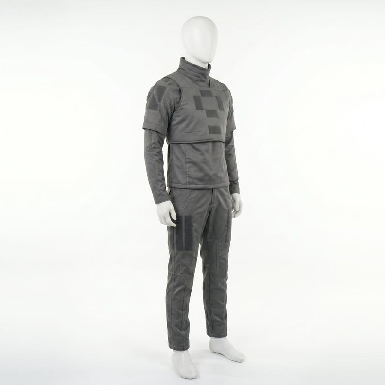 May include: A gray uniform displayed on a mannequin. The outfit includes a long-sleeved top with a high collar and a checkered pattern on the chest, along with matching pants. The uniform has several square patches.