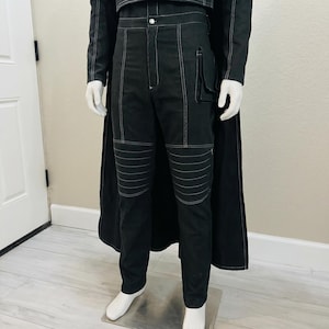 May include: Black pants with white stitching and a matching jacket are displayed on a mannequin. The pants have a pocket on the right leg and horizontal stitching on the knees. The jacket has white stitching and a button closure. A black cape is draped behind the outfit.