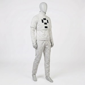 Puede incluir: Un traje futurista gris claro exhibido en un maniqu&iacute;. El atuendo incluye una parte superior de cuello alto con un dise&ntilde;o de cuadrados negros, mangas largas y pantalones a juego. La tela parece texturizada.