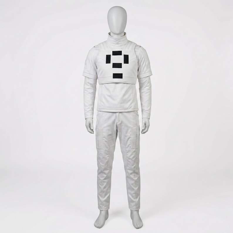 Puede incluir: Un traje blanco completo sobre un maniqu&iacute;. El atuendo incluye una parte superior de manga larga con cuello alto, una pieza en el pecho con detalles rectangulares negros y pantalones a juego con bolsillos de carga. El maniqu&iacute; est&aacute; sobre un fondo blanco.