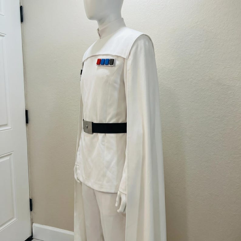 Puede incluir: Un disfraz blanco con cuello alto, mangas tipo capa y cintur&oacute;n negro. El uniforme presenta una serie de insignias rectangulares de colores en el pecho. El disfraz se exhibe en un maniqu&iacute;.