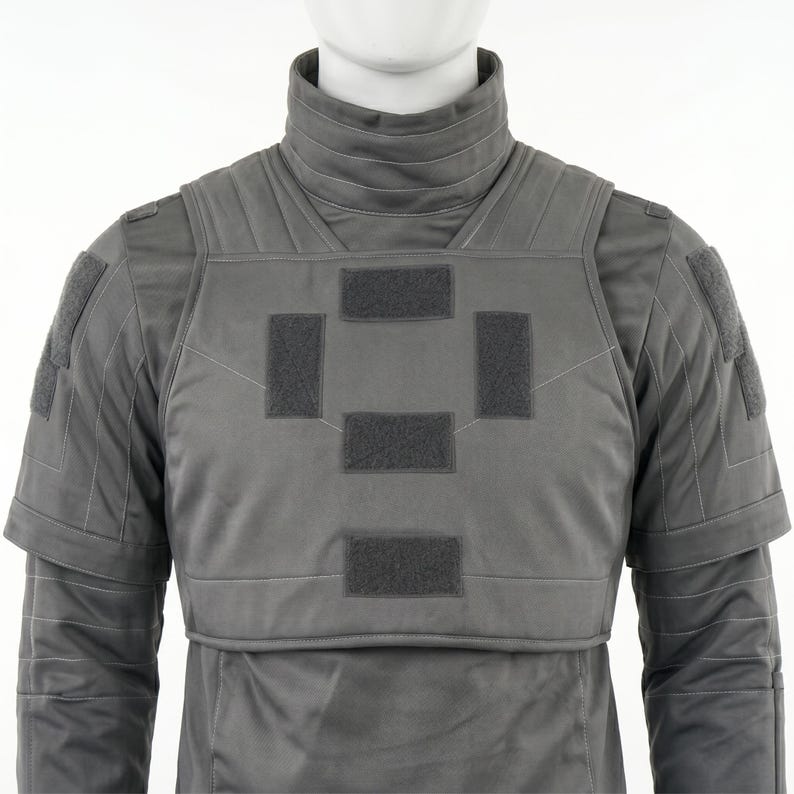 May include: A gray tactical vest with a high collar and multiple rectangular patches. The vest has a padded design and is worn over a long-sleeved garment. The overall aesthetic suggests a military or futuristic theme.