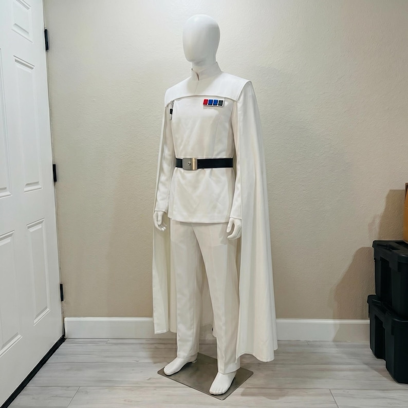 Puede incluir: Un disfraz blanco con capa, cintur&oacute;n y pantal&oacute;n. El disfraz tiene un cuello alto y una serie de rect&aacute;ngulos de colores en el pecho. El cintur&oacute;n es negro con una hebilla plateada. El disfraz se exhibe en un maniqu&iacute;.