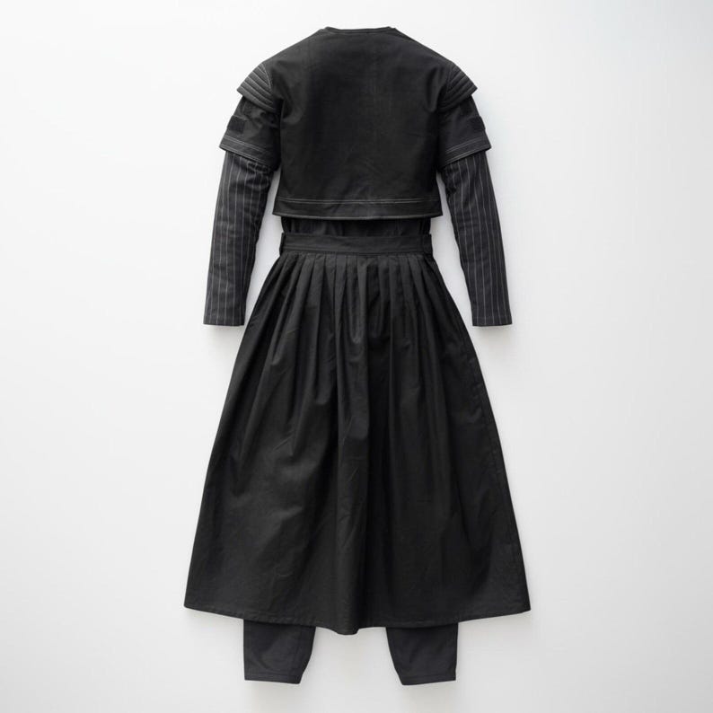 May include: A black outfit comprising a cropped jacket, a long-sleeved shirt with pinstripes, a pleated skirt, and matching trousers. The jacket has a round neckline and layered sleeves. The skirt is long and flowing, and the trousers are straight-legged.