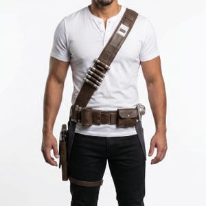 May include: A brown leather utility belt with multiple pouches, a holster, and a shoulder strap with silver bullet-shaped details. The belt is worn over black trousers and a white Henley shirt. A leg strap is also visible.