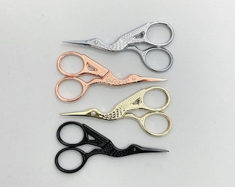 May include: Four pairs of decorative scissors with bird-shaped handles. The scissors are silver, rose gold, gold, and black.