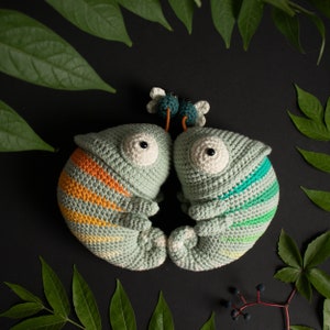 Puede incluir: Dos peluches de camale&oacute;n de crochet verde con detalles en naranja y azul. Los peluches se miran y tienen ojos grandes y blancos.