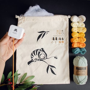 Puede incluir: Un kit de manualidades para hacer un camale&oacute;n de peluche. El kit incluye una bolsa de lona blanca con una ilustraci&oacute;n en blanco y negro de un camale&oacute;n en una rama, una peque&ntilde;a caja de relleno, una aguja, hilo, botones y una variedad de hilos de colores.