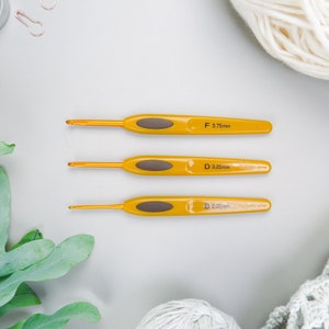 Puede incluir: Tres agujas de crochet amarillas con mangos marrones. Las agujas están etiquetadas con sus tamaños: F 3,75 mm, D 3,25 mm y B 2,25 mm. Las agujas están hechas por Clover Japan.