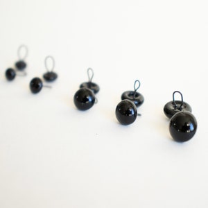 May include: Six black plastic safety eyes with wire loops for attaching to crafts. The eyes are different sizes.