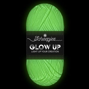 Può includere: Un gomitolo di filato verde che brilla al buio con un'etichetta che recita "Scheepjes Glow Up Light Up Your Creation."